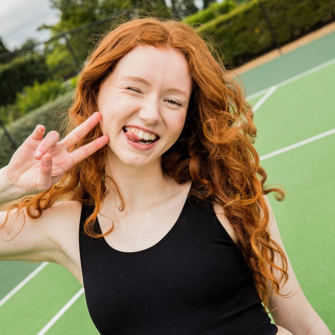 Girl with red hair smiling and holding up her fingers in a peace sign