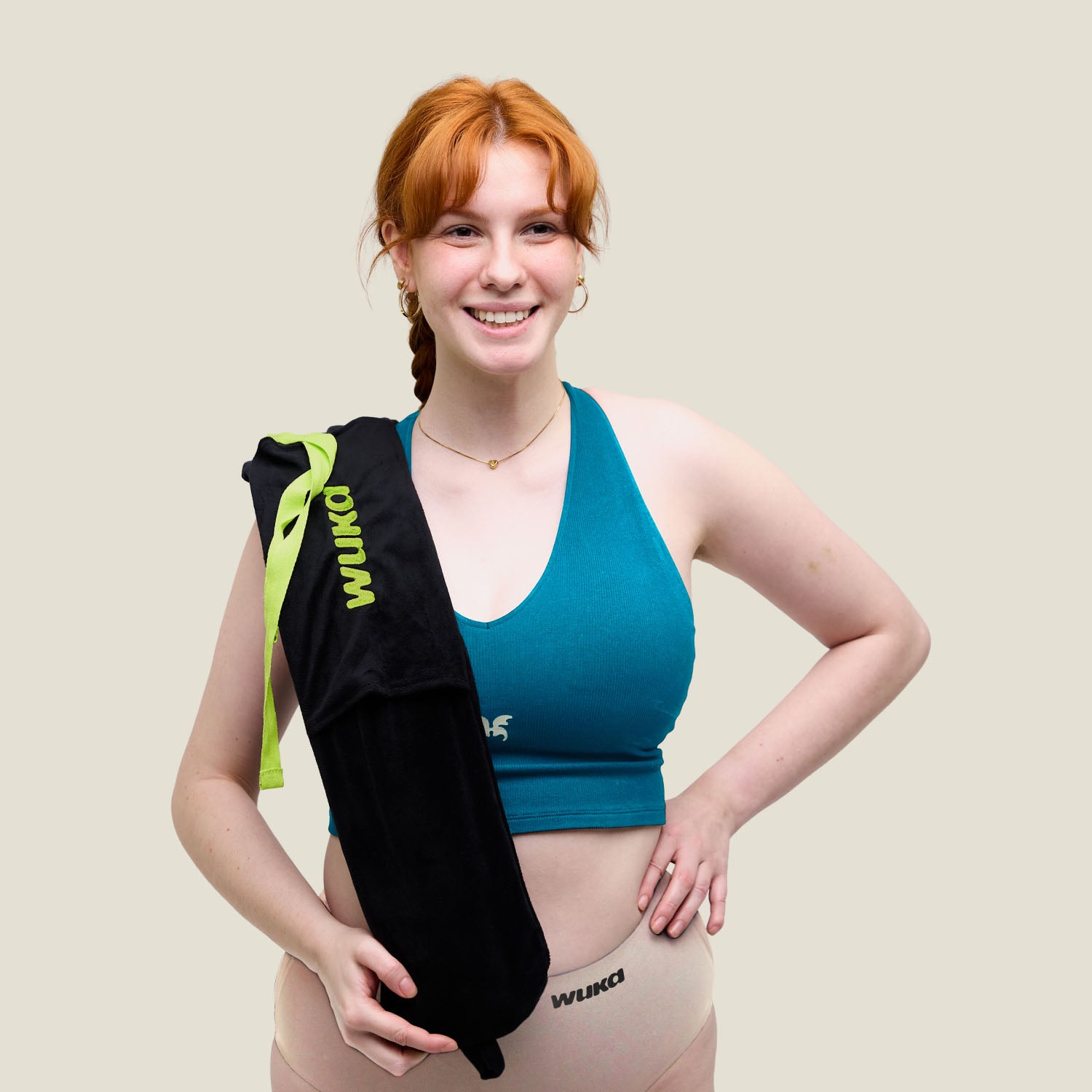 Smiling model holding WUKA’s soft fleece-covered long hot water bottle over shoulder, wearing WUKA period pants and teal top