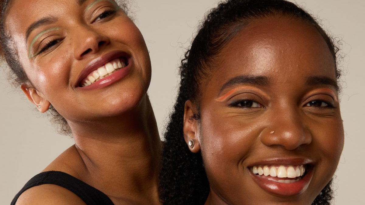 Two women smiling close to each other against a neutral background